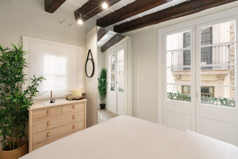 A bedroom with white walls and wooden beams.