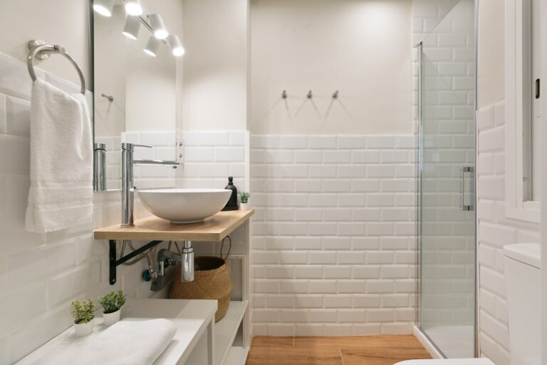 A bathroom with white tile and wood floors.