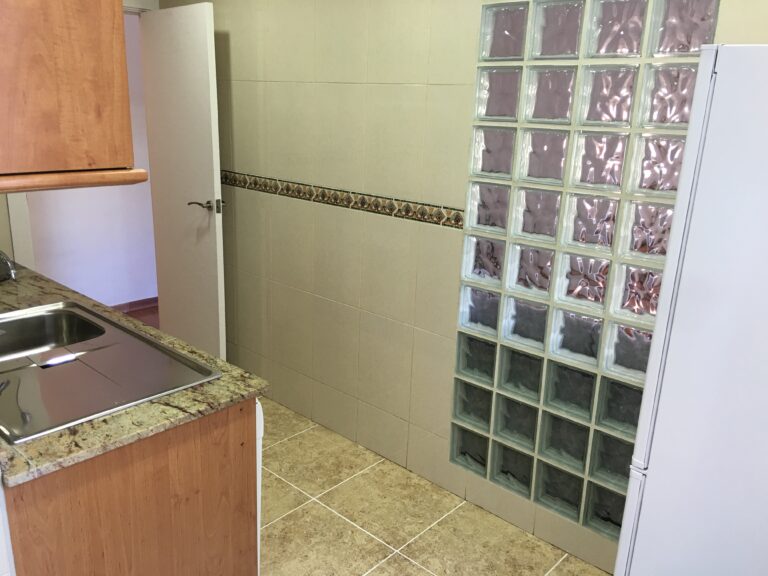 A kitchen with tile floors and a glass block wall.